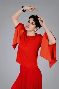 Dynamic creative portrait by Chaplin Studio featuring a woman in a vibrant red outfit with flared sleeves, striking an expressive pose.