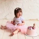 Adorable girl in pink outfit enjoying a smash cake with pink frosting — joyful birthday portrait by Chaplin Studio