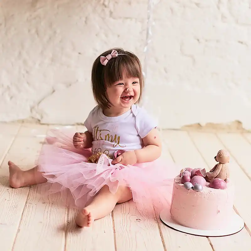 Adorable girl in pink outfit enjoying a smash cake with pink frosting