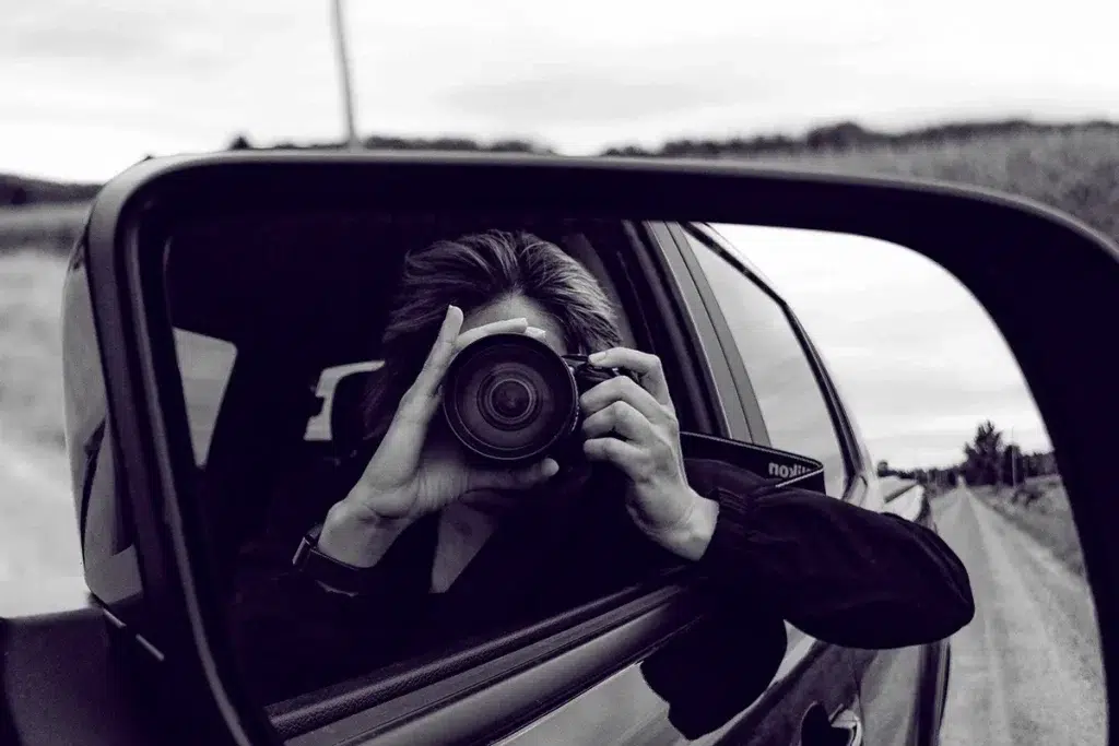 Black and white reflection of a wedding photographer in a car's side mirror.