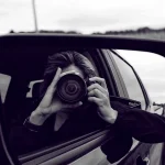 Black and white reflection of a wedding photographer in a car's side mirror.