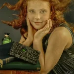 A young girl with red hair and freckles poses with old books and a decorative box, perfect for creative child portrait photography by Chaplin Studio in Yorkshire.