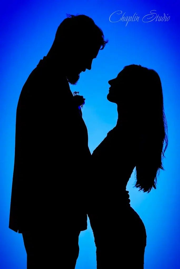 Silhouette of a bride and groom facing each other against a glowing blue background
