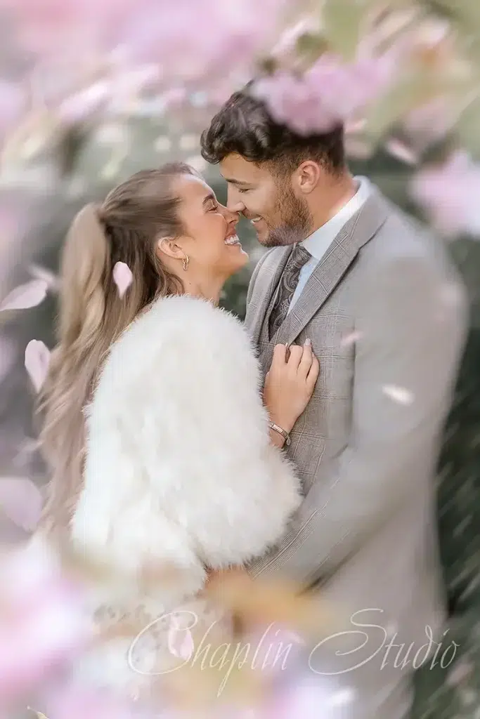 A romantic and joyful wedding portrait of a newlywed couple embracing, with soft pink floral elements in the foreground, captured by Chaplin Studio in Yorkshire.