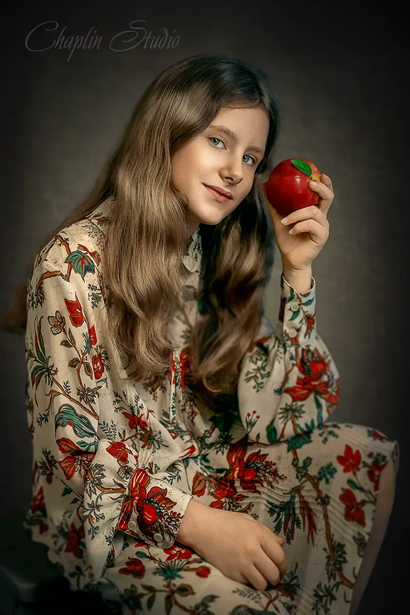 Beautiful child portrait of a girl in a floral dress holding a red apple, fine art style by Chaplin Studio.