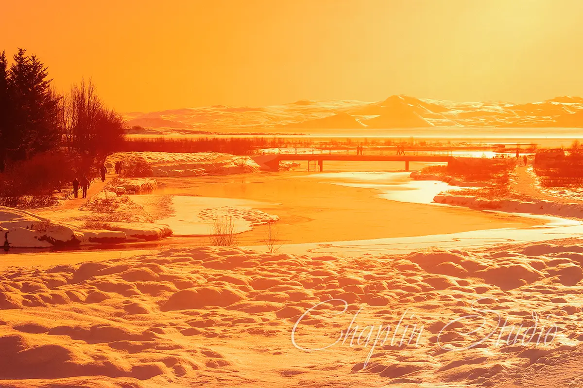 Stunning winter landscape bathed in golden hour light, featuring a frozen river and bridge, perfect for nature travel photos.