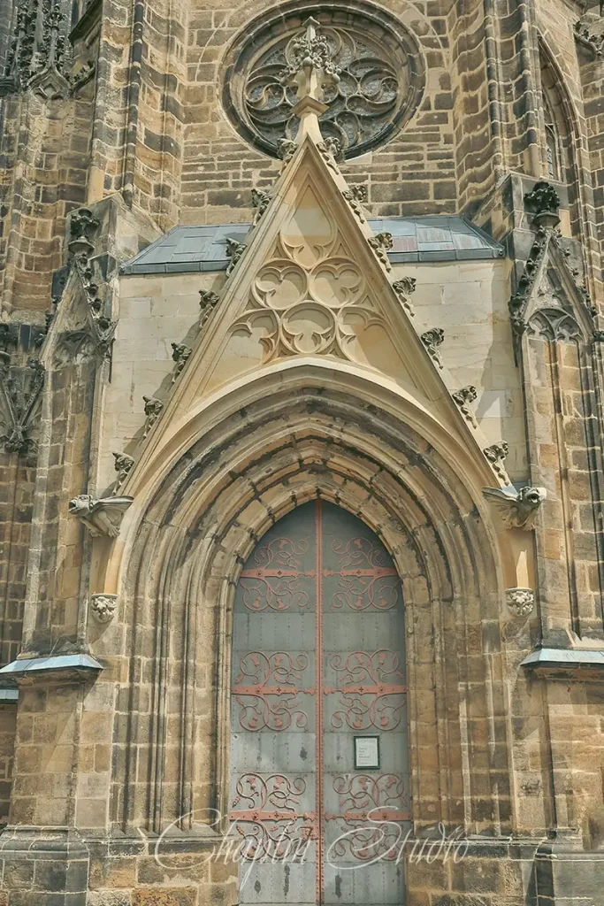 Close-up of a grand Gothic church entrance with an ornate, metal double door, intricate stone carvings, a rose window above, and detailed architectural elements, captured by Chaplin Studio.