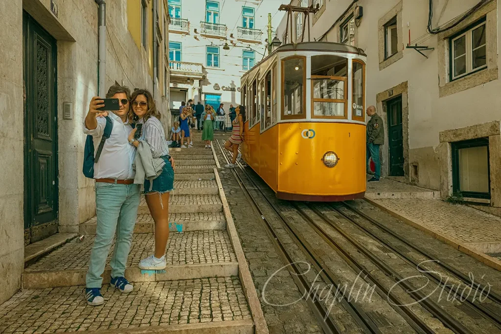 A couple taking a selfie on a cobblestone street in Lisbon, Portugal, with a classic yellow tram in the background, captured by Chaplin Studio for vibrant travel photography.