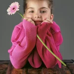 Little girl in a pink dress with a flower, leaning on an antique chest – fine art portrait by Chaplin Studio