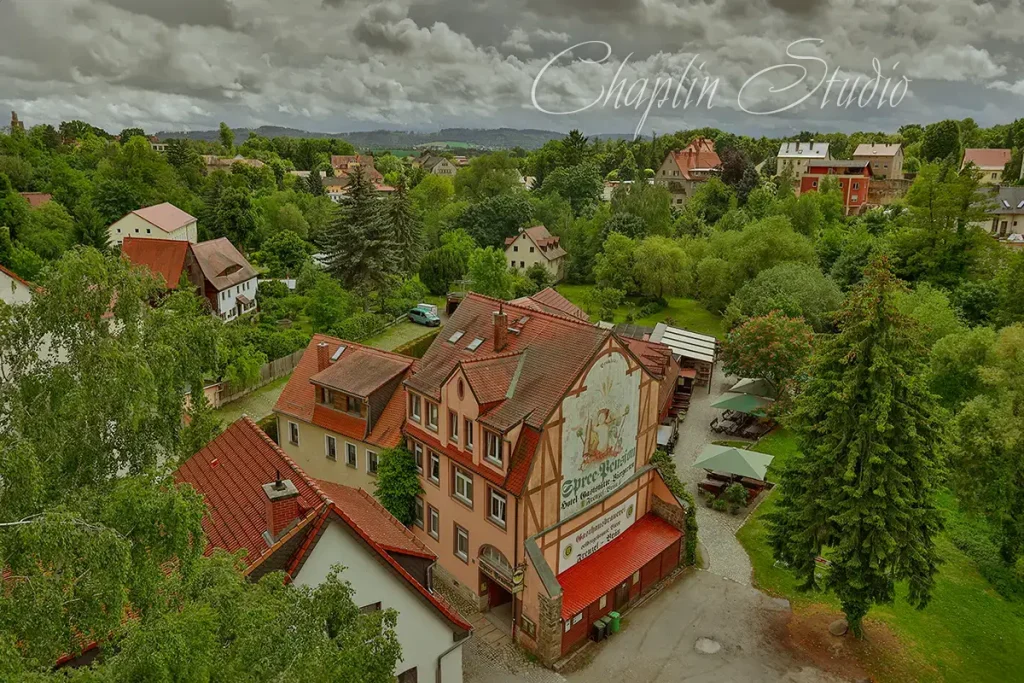 Aerial view of a charming historic German town with red-tiled roofs, lush green trees, and a building featuring a painted mural, captured by Chaplin Studio.