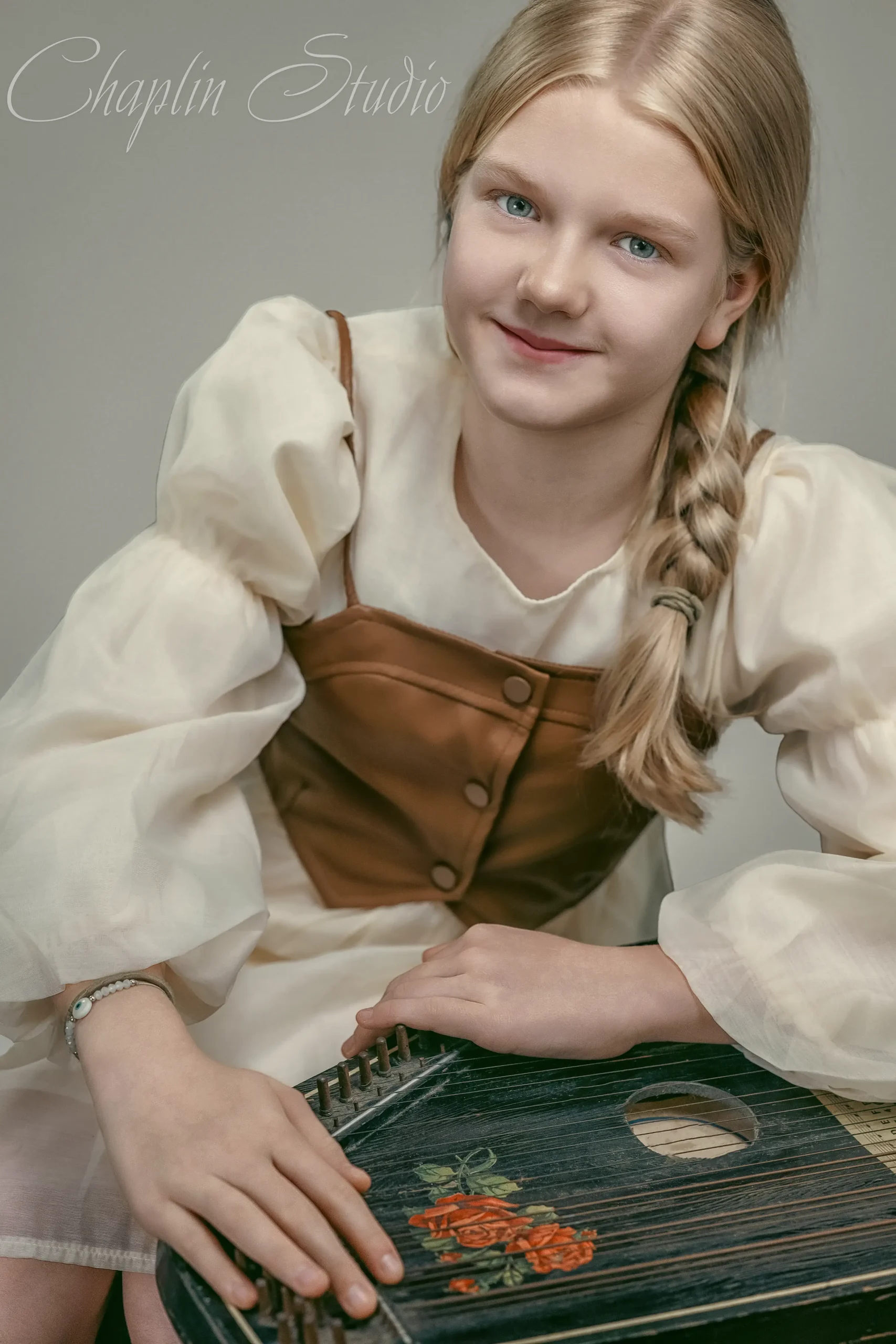 A young girl with blonde hair and a braid, wearing a historical-style dress and holding a stringed instrument, captured in a unique child portrait by Chaplin Studio in Yorkshire.