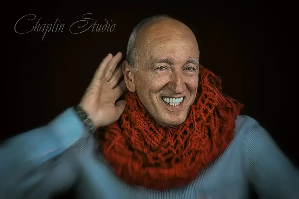 An expressive studio portrait of a man with a warm smile, wearing a large red knitted scarf and light blue shirt, captured with dynamic lighting by Chaplin Studio in Yorkshire.