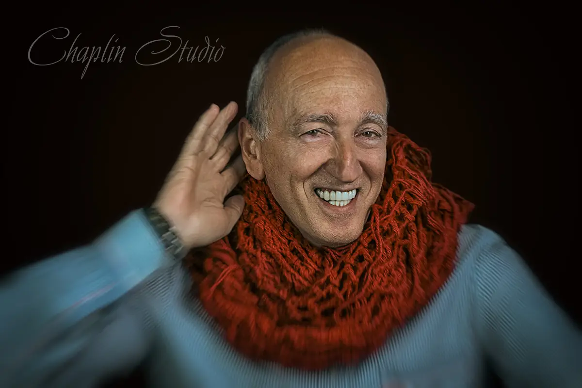 An expressive studio portrait of a man with a warm smile, wearing a large red knitted scarf and light blue shirt, captured with dynamic lighting by Chaplin Studio in Yorkshire.