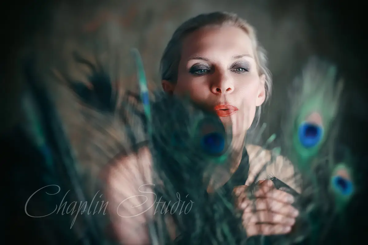 An artistic studio portrait of a woman with light hair, blowing through peacock feathers, creating a dramatic and expressive image by Chaplin Studio in Yorkshire.