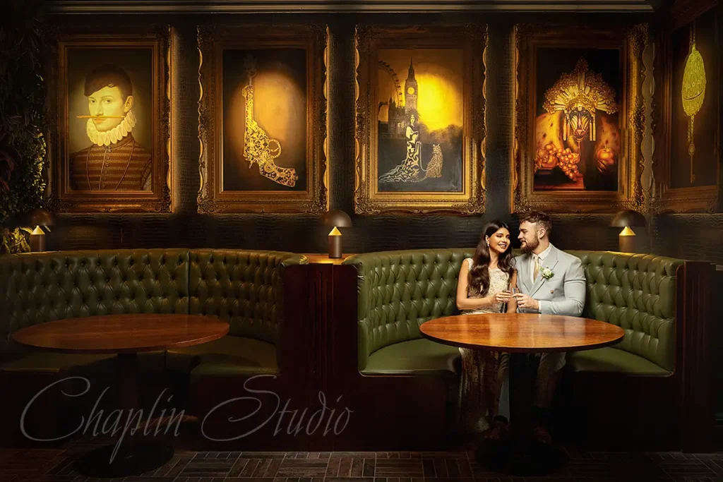 A stylish wedding couple in a luxurious, dimly lit lounge with ornate framed paintings on the wall, captured by Chaplin Studio, a Yorkshire Wedding Photographer.