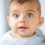 Adorable baby with bright blue eyes in a soft natural light portrait wearing a pastel knitted outfit