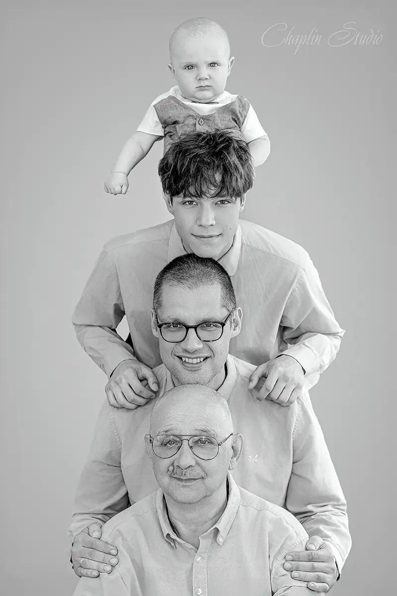 Black and white studio portrait of a four-generation family, from baby to great-grandfather, posing vertically.